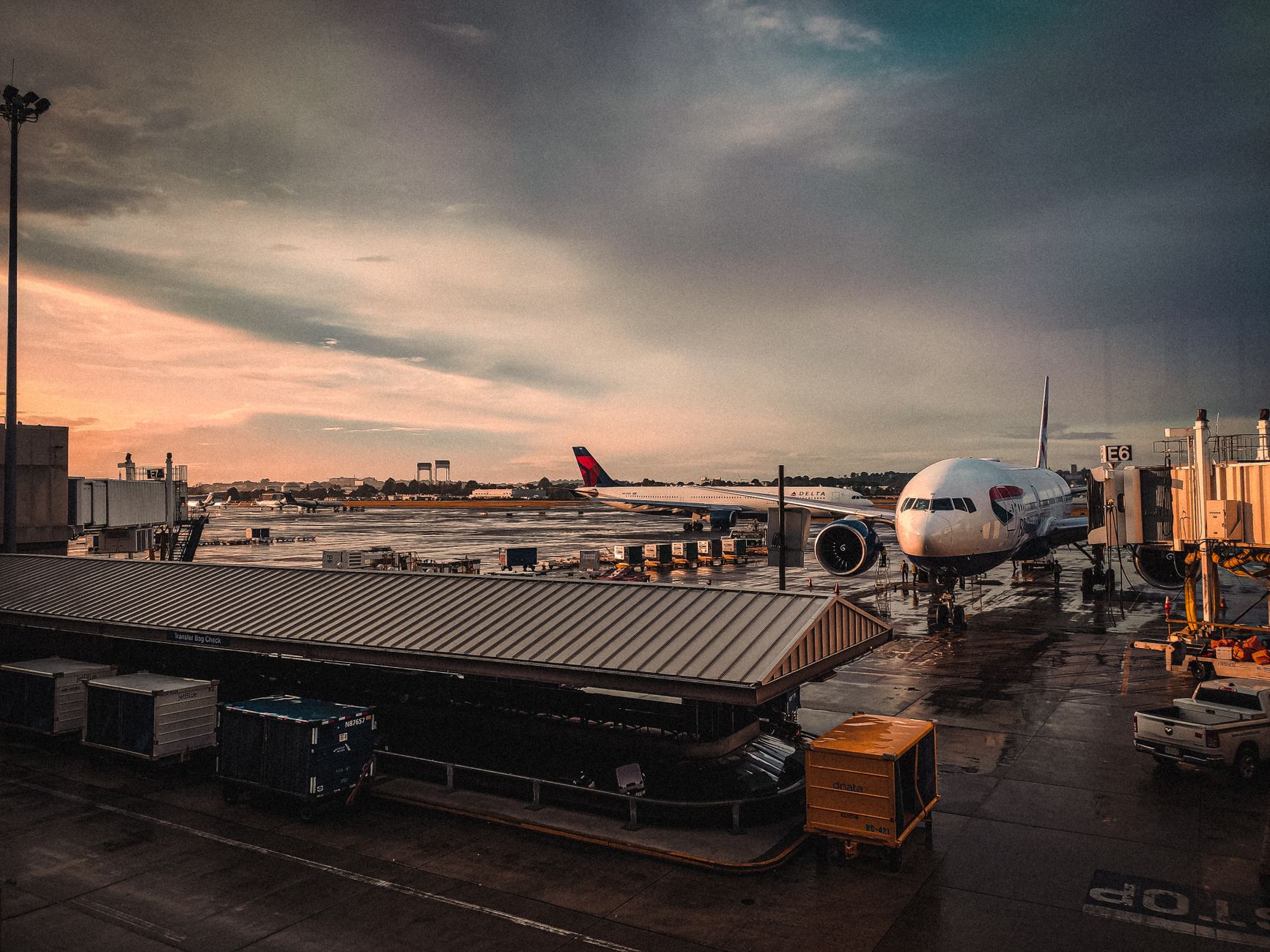 An airplane parked at an airport gate during sunset with reflections on wet tarmac.