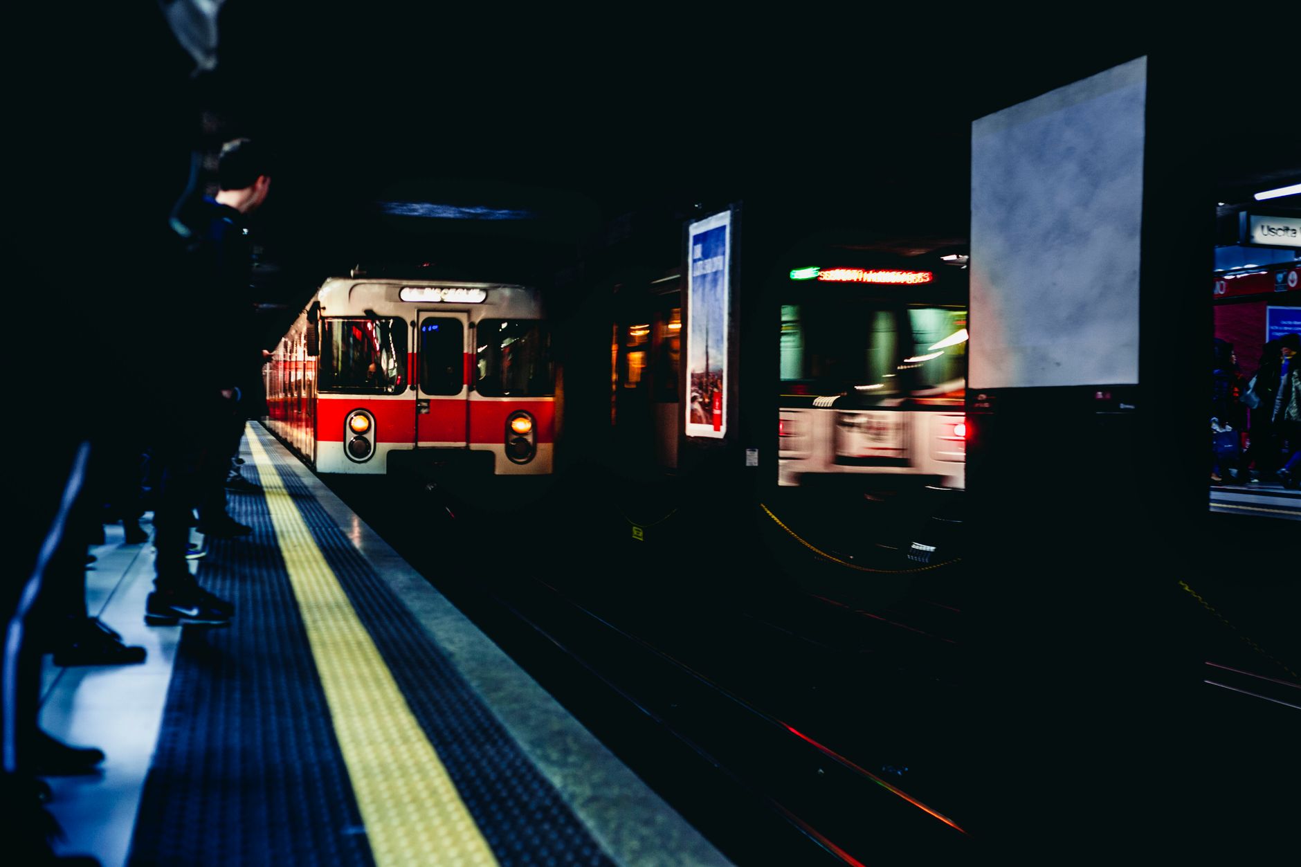 Urban night scene of a train arriving at a Milan subway station, capturing movement and city life.