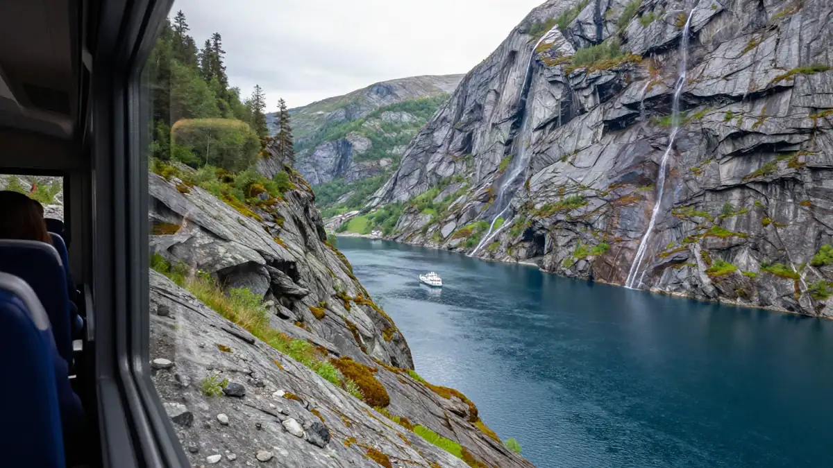 Blick vom Zugfenster auf einen tiefblauen Fjord mit steilen Felswänden
