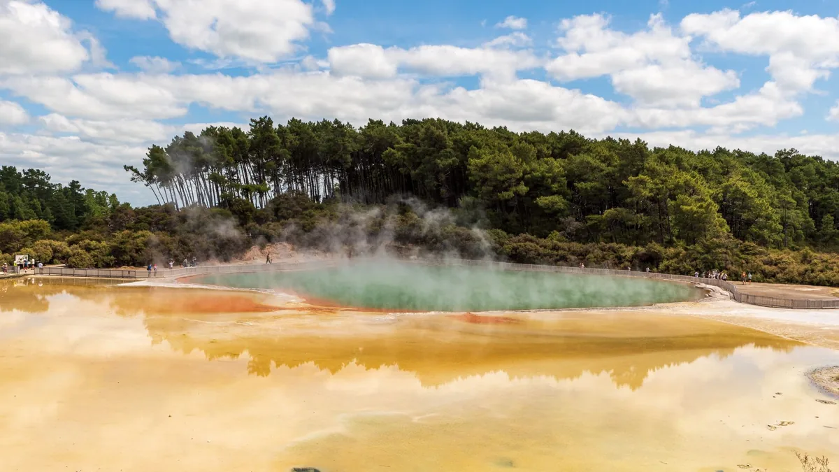 Dampfende Geothermalquellen mit rotbrauner Erde und türkisfarbenen Pools im Vordergrund