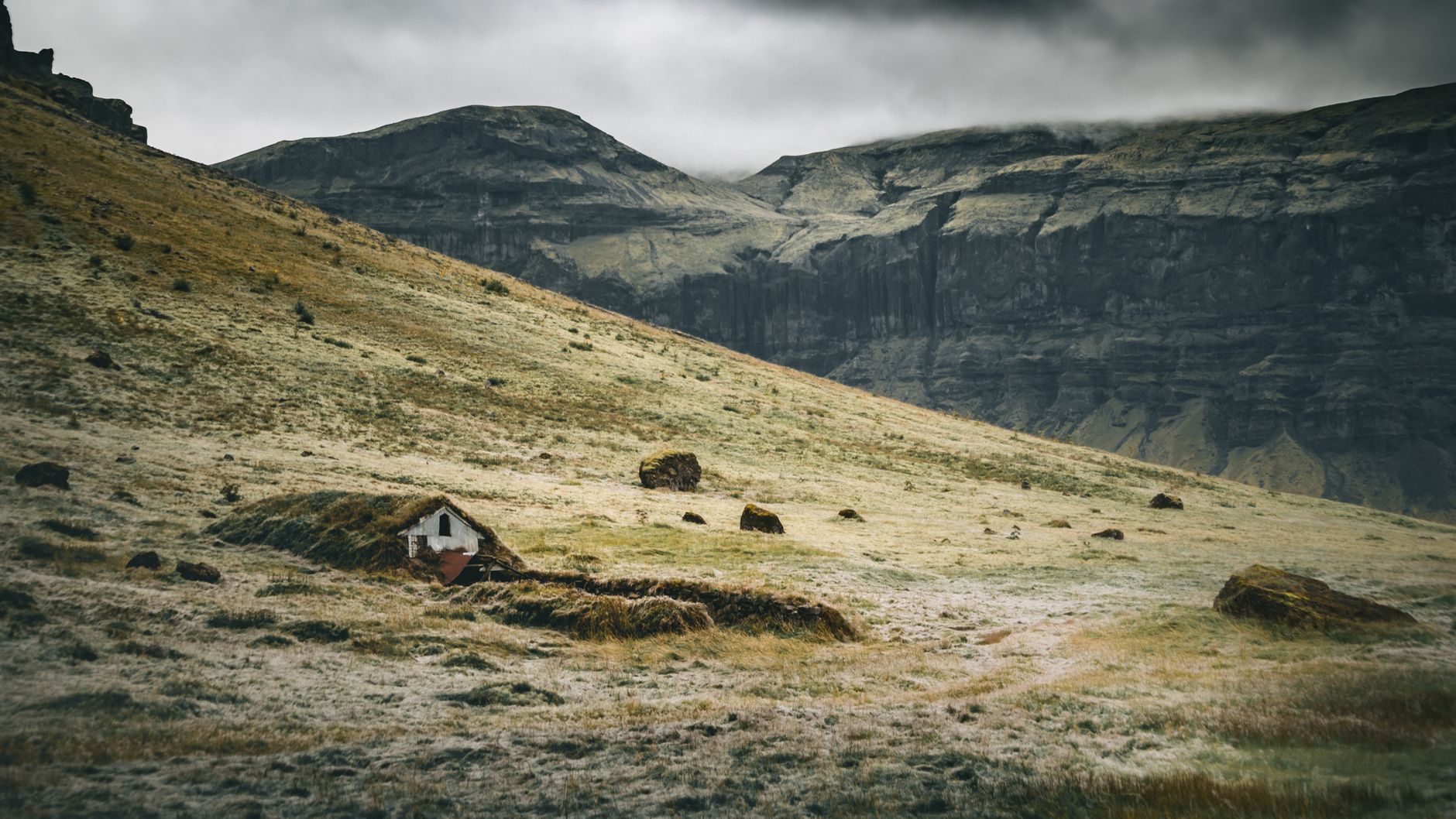 A beautiful Icelandic landscape featuring a traditional turf house under dramatic skies.