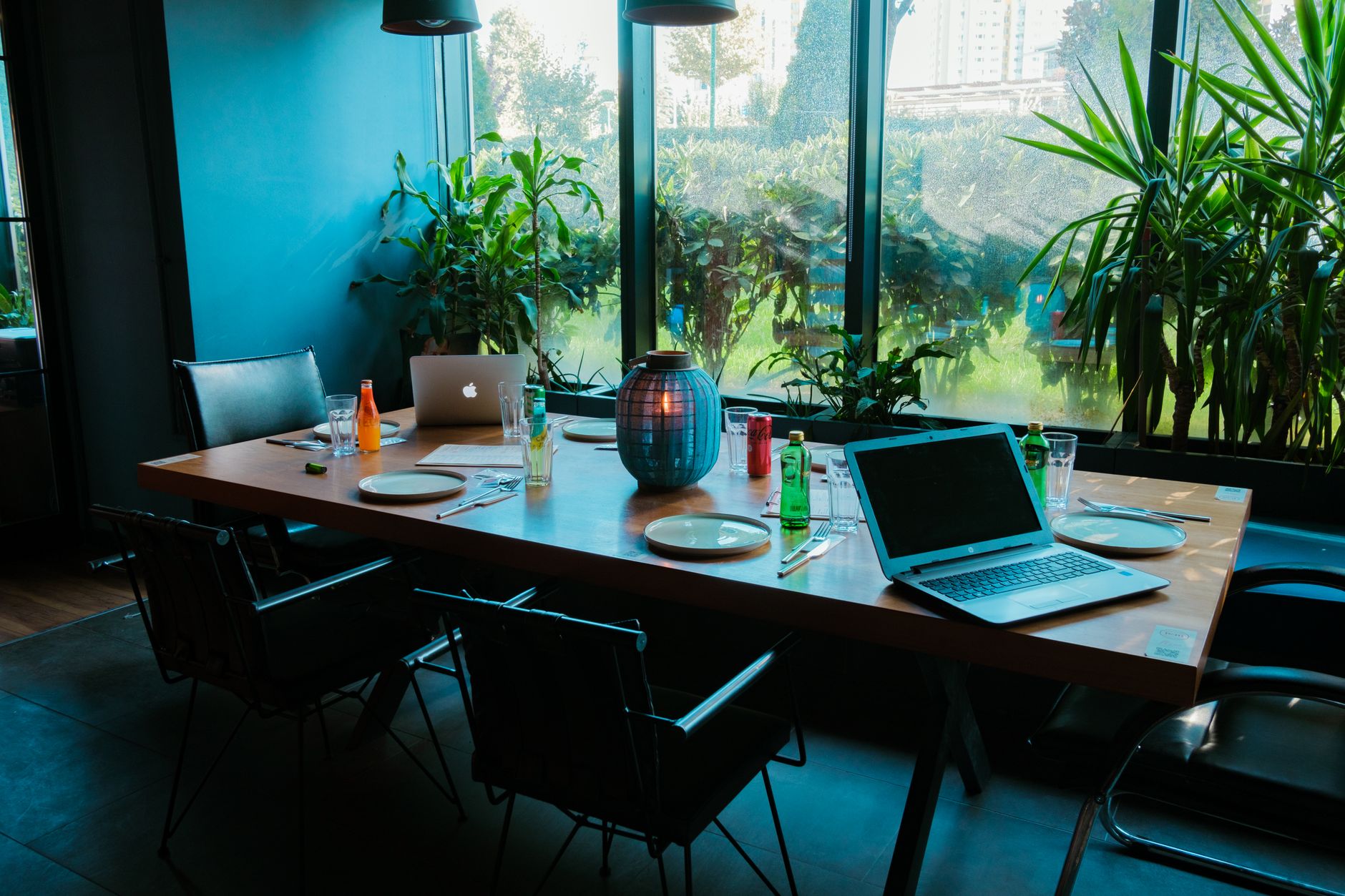 Modern office meeting room with laptops, drinks, and lush greenery.