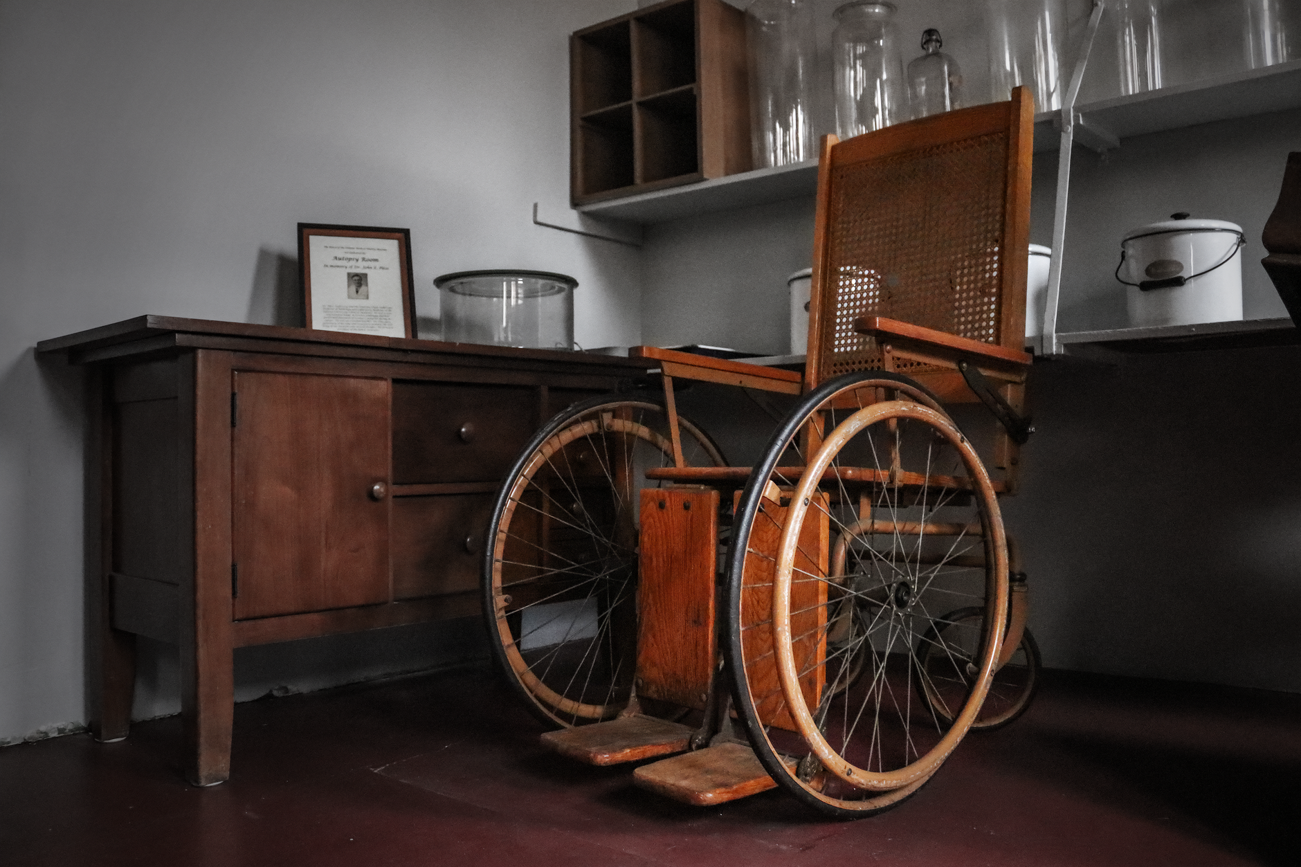 Antique wooden wheelchair alongside vintage furniture in historical interior setting.