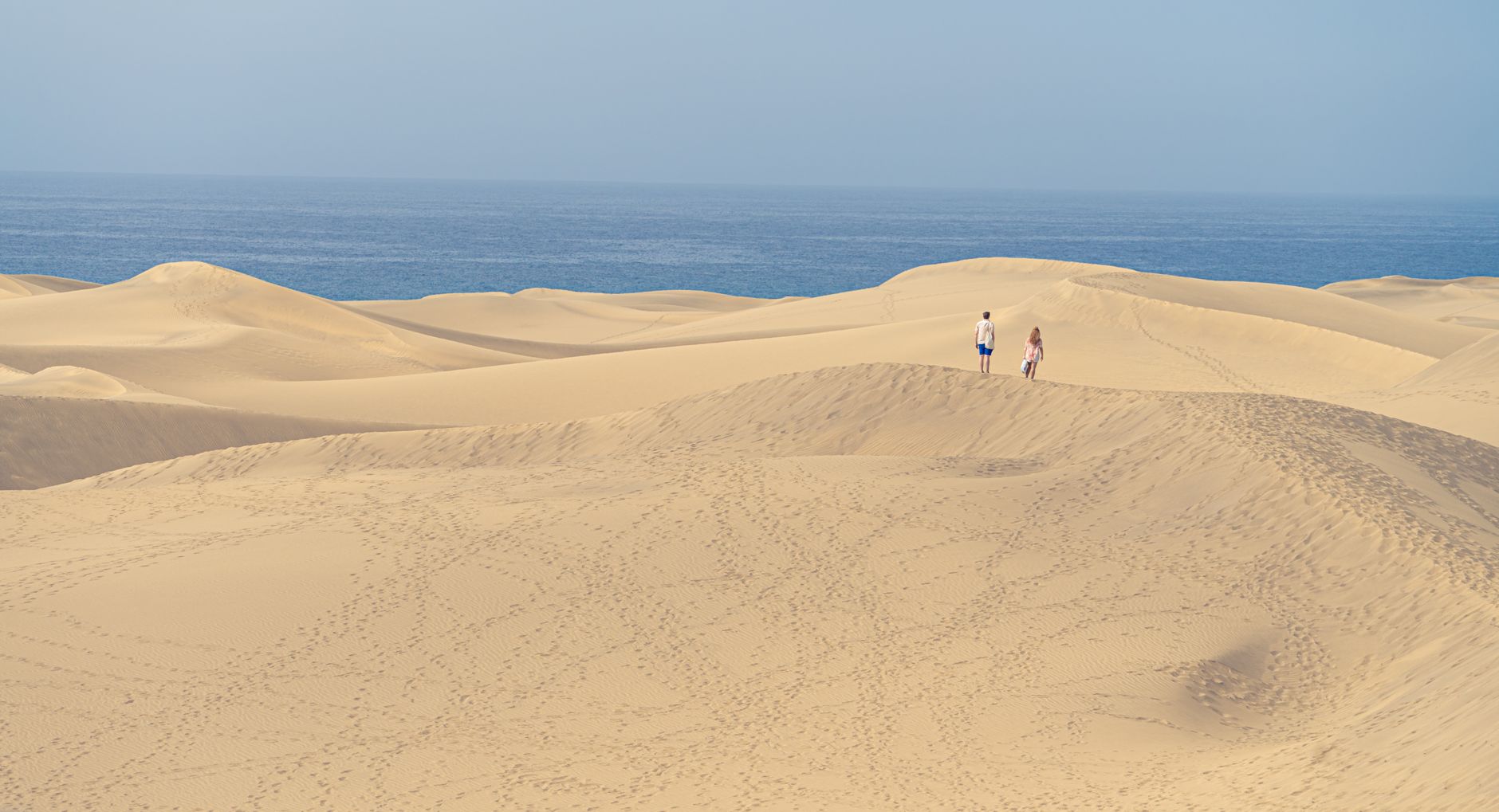 Peaceful dunes of Maspalomas in Spain with ocean views and two people exploring.