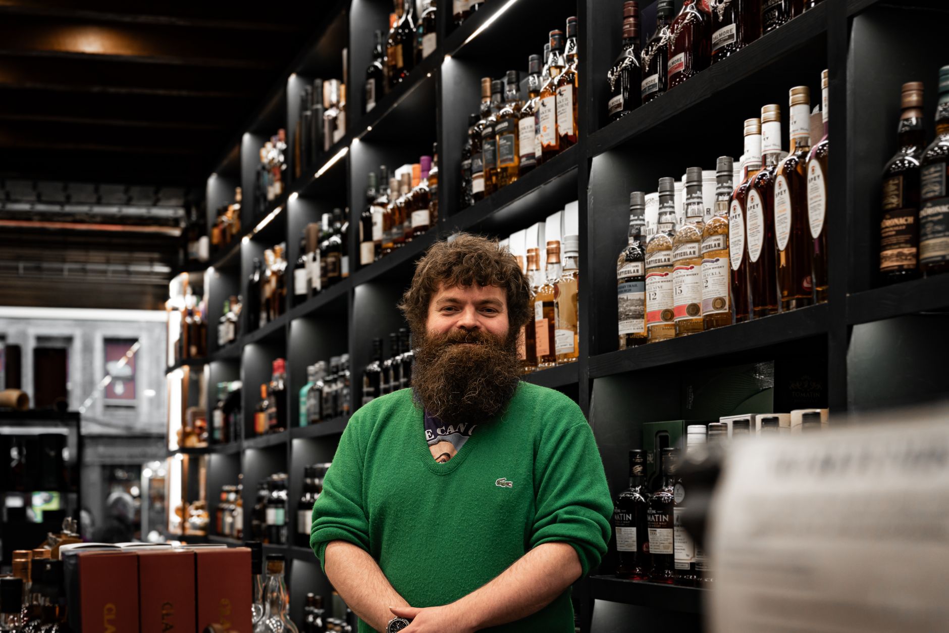 Smiling bartender in a whisky store in Edinburgh, Scotland with shelves of bottles.