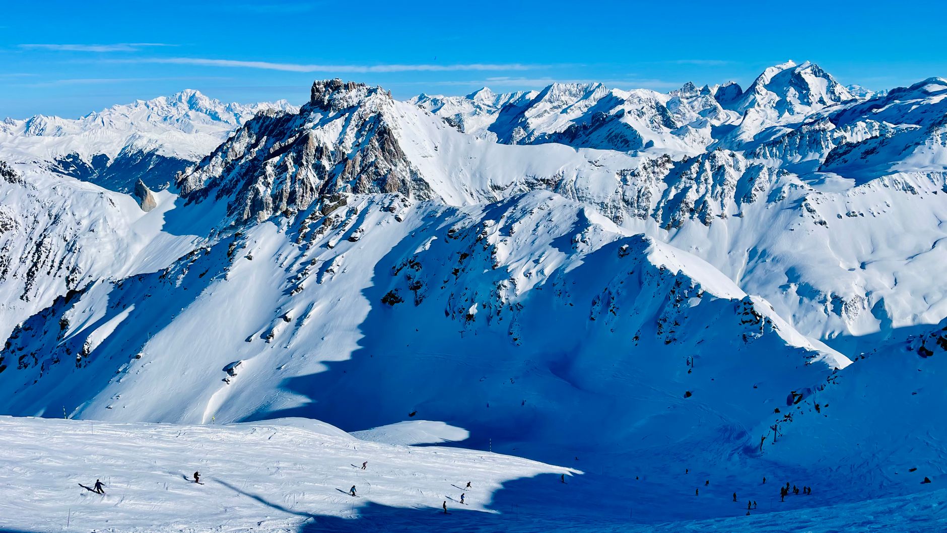 A breathtaking view of skiers on snow-covered Alps with clear blue skies.