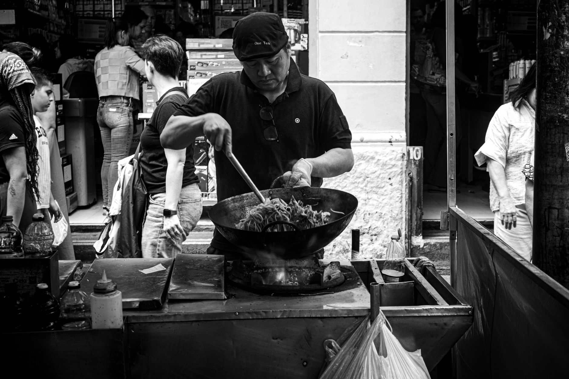A street food vendor skillfully cooking noodles in a busy market setting.