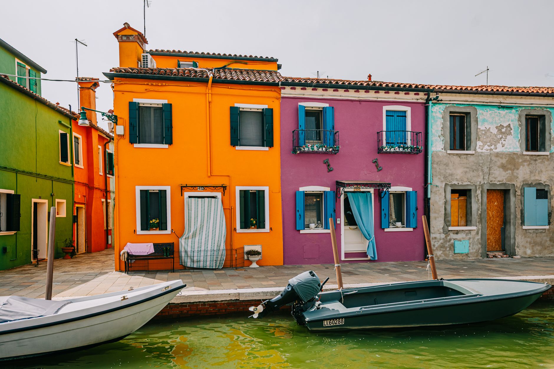 Vibrant houses along a canal in Burano, Venice with colorful facades and moored boats.