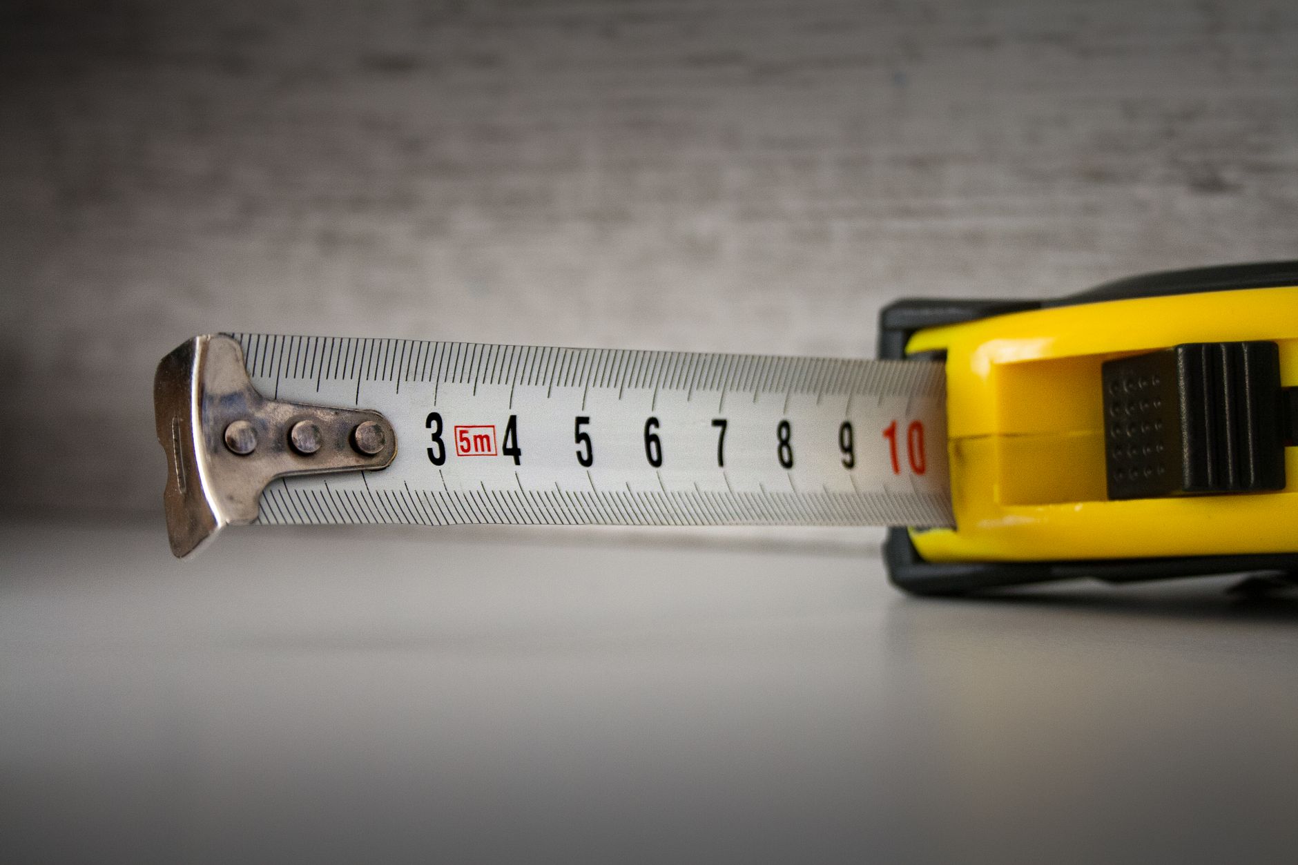 Detailed image of a yellow tape measure extended to 10cm on a neutral background.