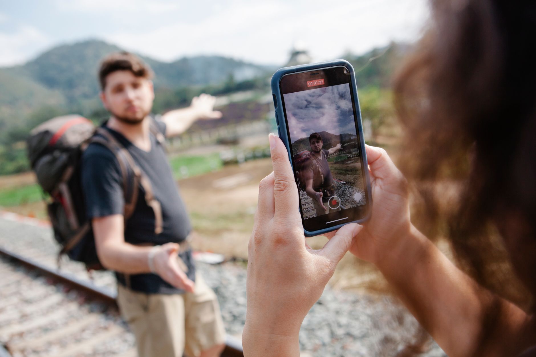 Crop unrecognizable female taking video on smartphone of hiker in casual clothes with backpack stand