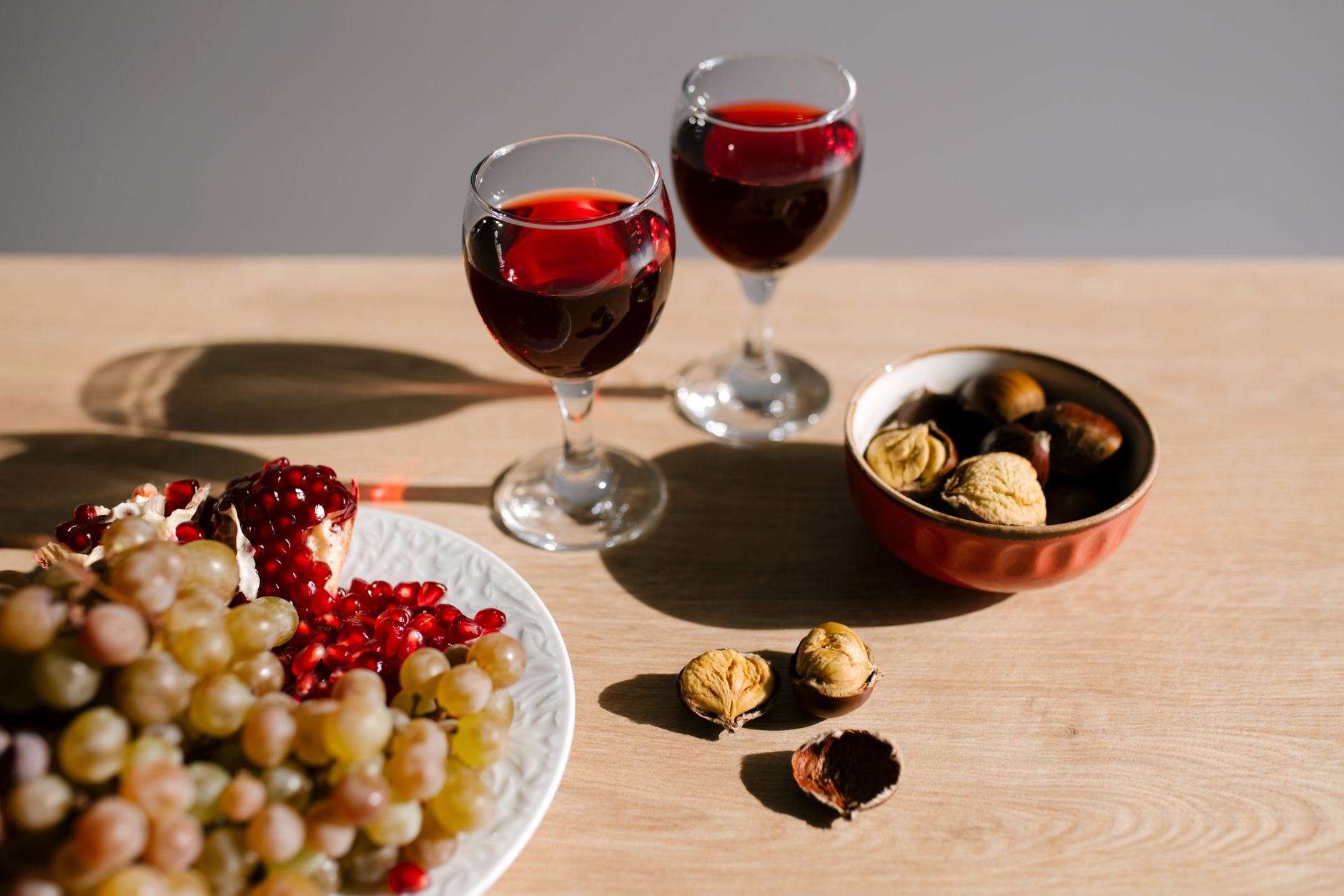 A sophisticated still life featuring red wine glasses, grapes, and nuts on a wooden table.