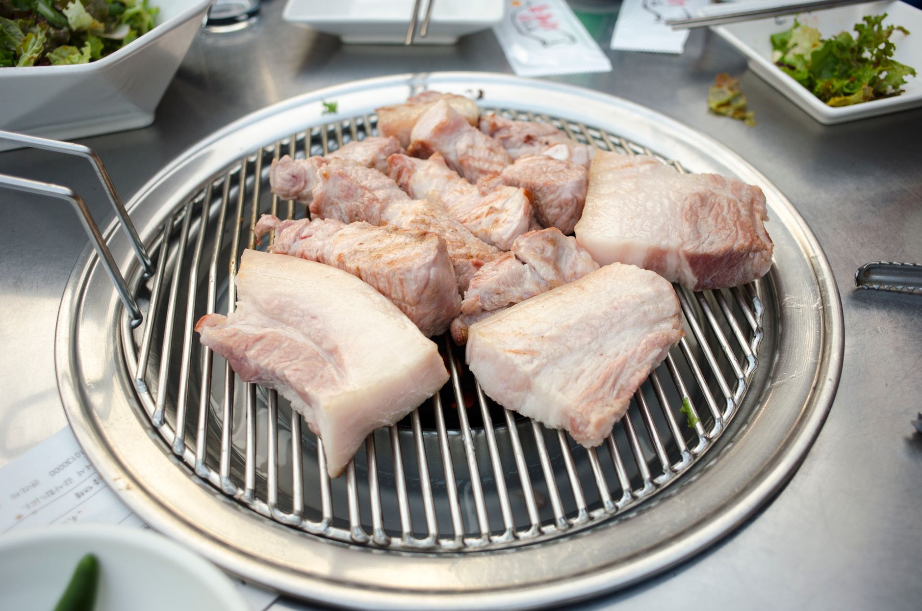 Raw pork pieces placed on a grill, ready for cooking, surrounded by side dishes.